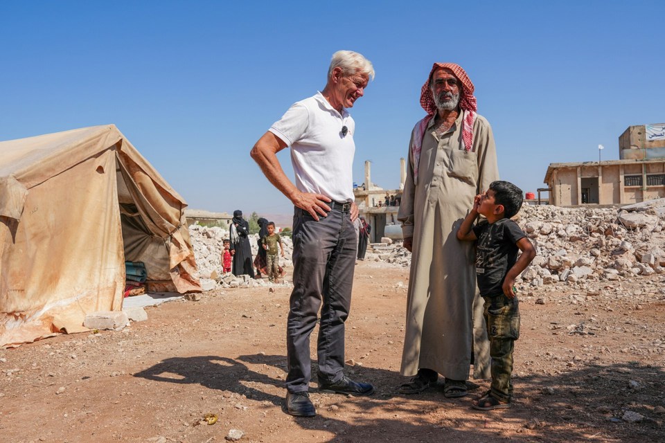 Jan Egeland står sammen med en mann og en liten gutt utenfor et telt i Syria. 