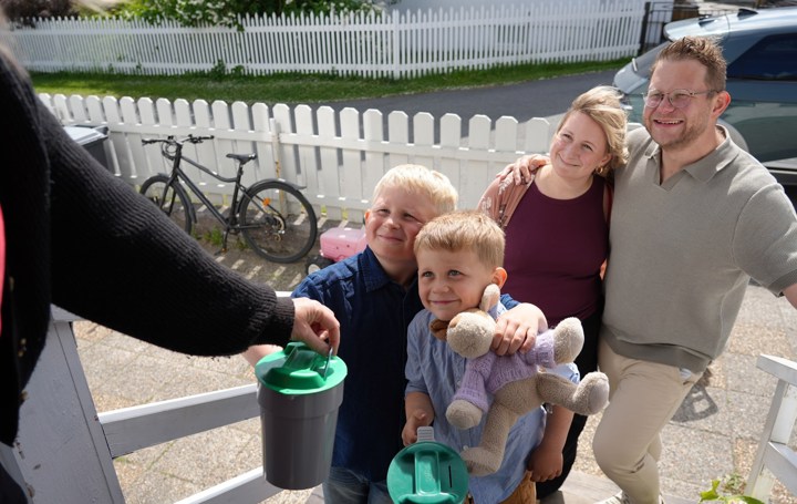 To voksne og to små gutter holder en bøsse. En dame gir penger på bøssa. 