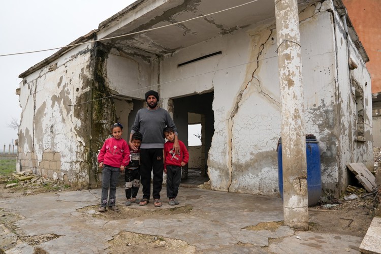 Hussin Faraj y sus tres hijos frente a su vivienda destruida por la guerra en Siria