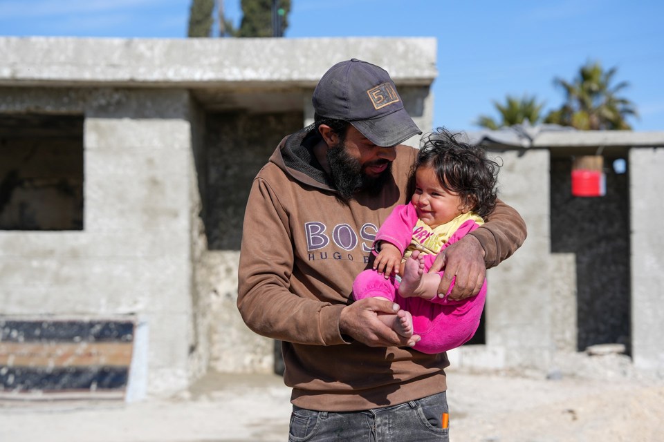 En mann med caps holder en latterfull jente i armene. 