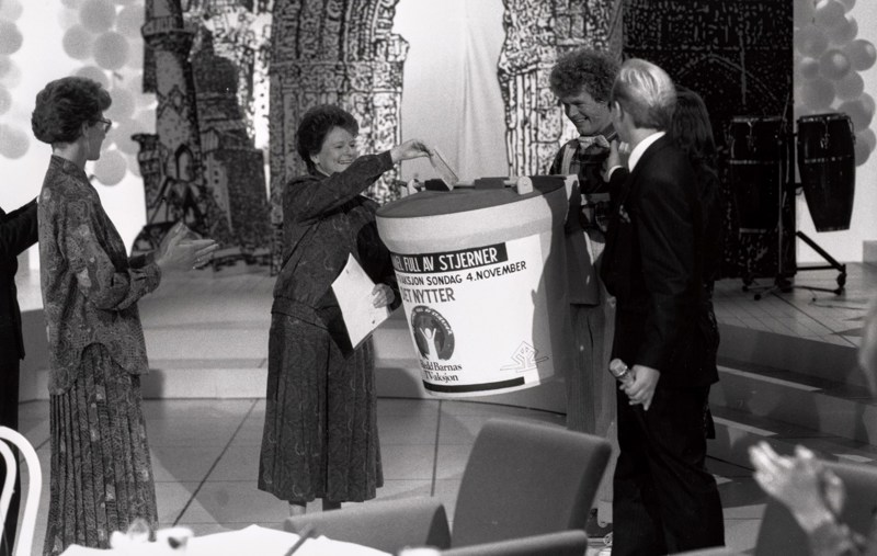 Gro Harlem Brundtland i studio i 1990, gir gave til TV-aksjonen på vegne av regjeringen. Hun putter en sjekk i en stor bøsse, og får applaus av folk rundt.
