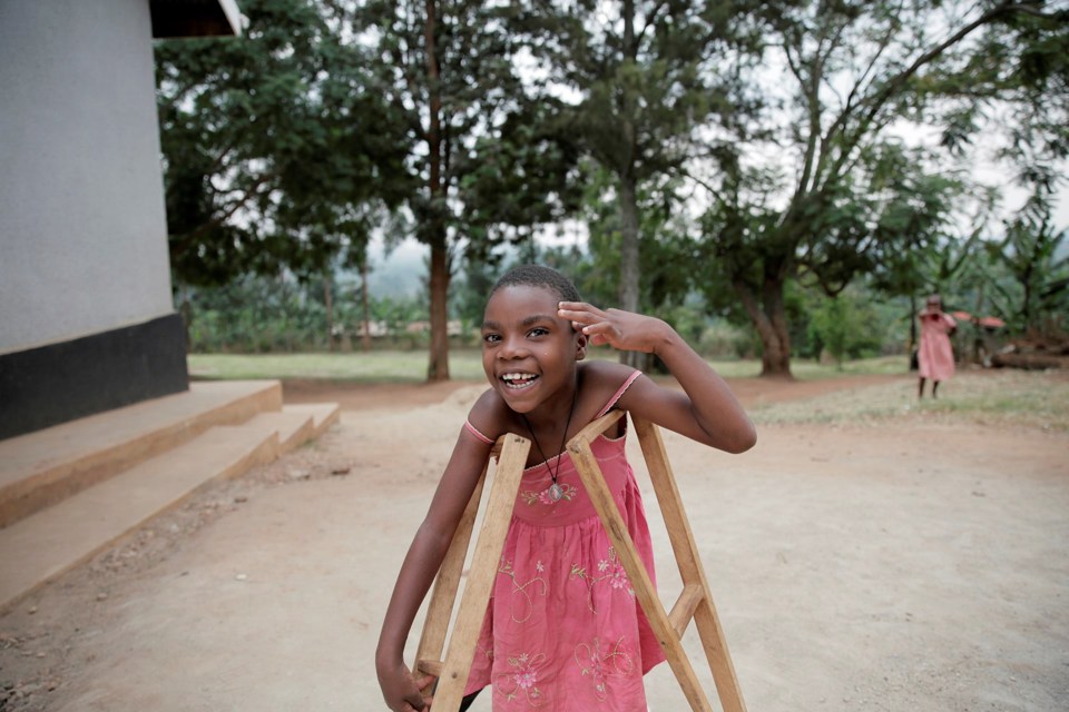 En smilende jente med rosa kjole står ute med krykker og løftet hånd. 